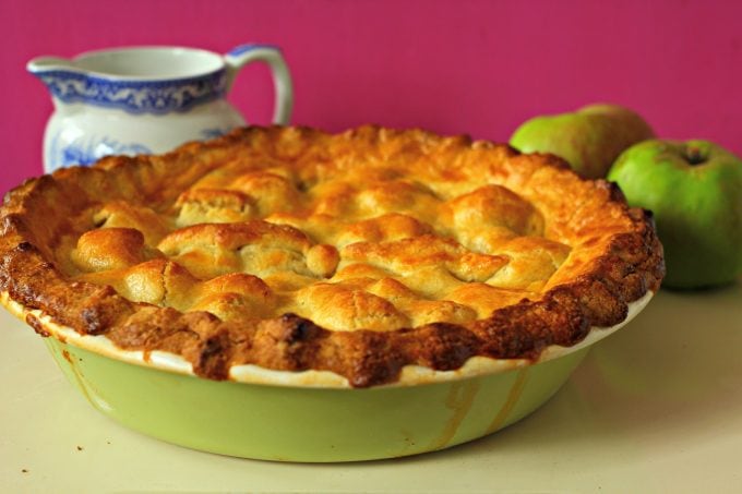 deep dish apple pie with a jug of cream and some raw apples