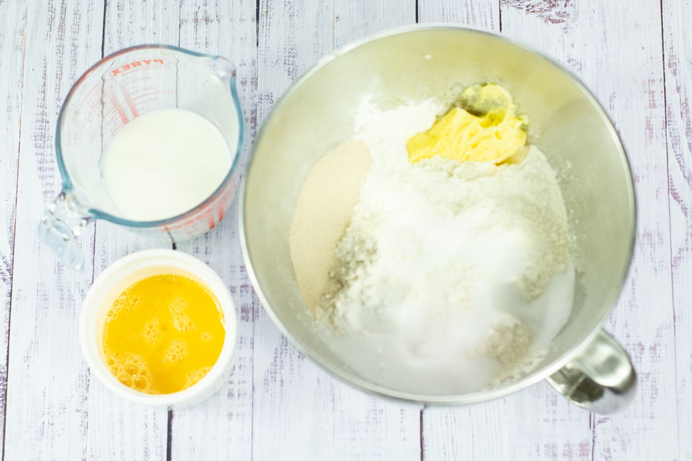 eggs, flour, sugar, butter, salt, dried yeast, milk and water in bowls on a white board