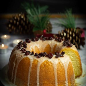 bundt cake topped with icing and cranberries on a plate with pine cones and tea lights behind