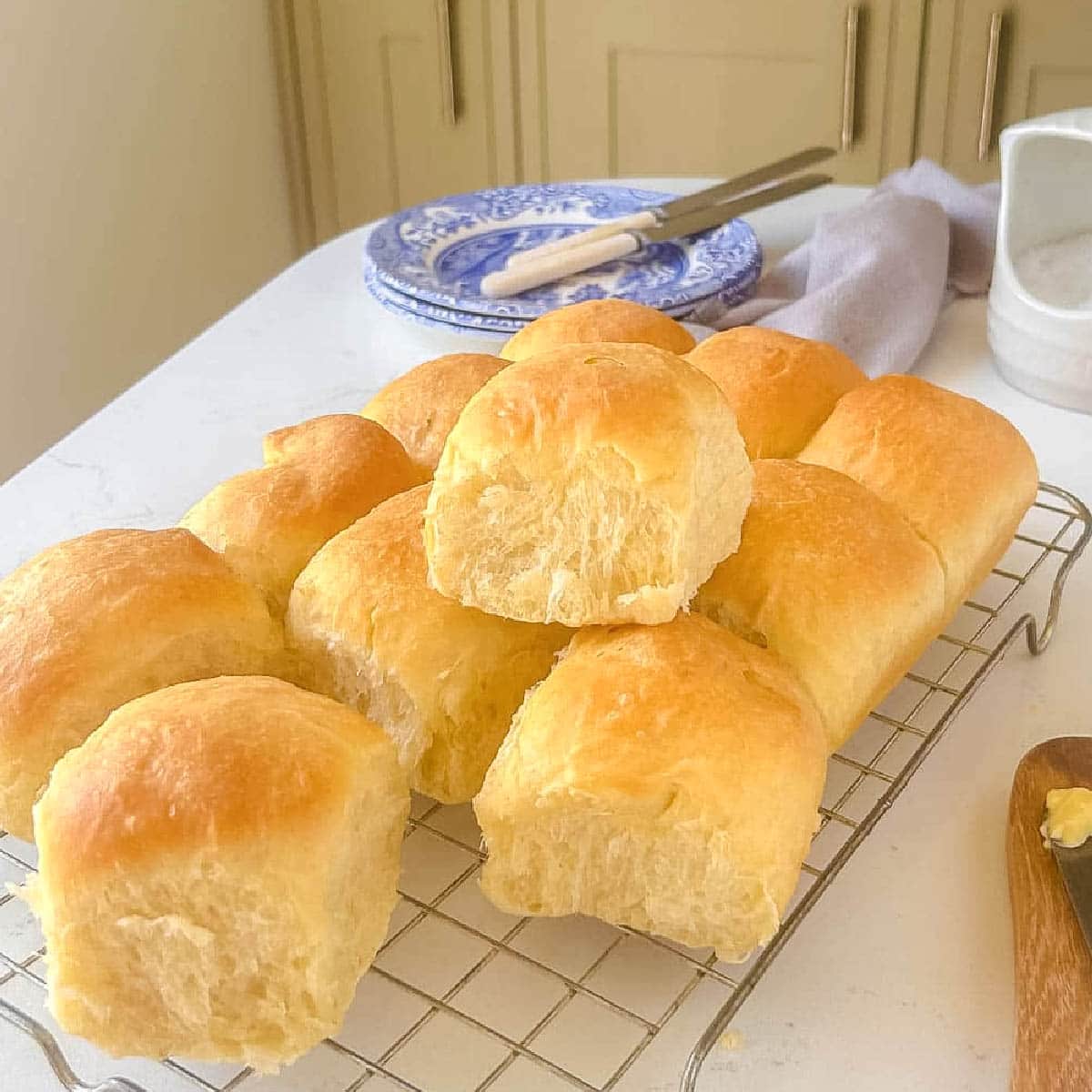 bread rolls on a wire rack with plates and butter knives in the background