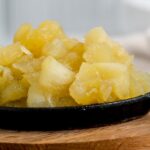 stewed apples piled high on a black serving dish on a wooden board