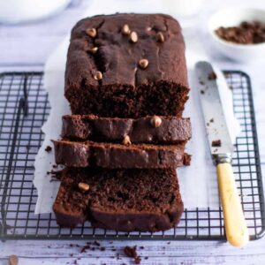 chocolate loaf cake on a wire rack with a orange handled knife to the side