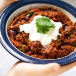 Slow Cooker Chilli Con Carne in a bowl with sour cream and coriander leaves