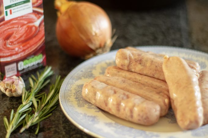 slow cooker sausage casserole ingredients Slow Cooker Sausage Casserole Ingredients with a plate of sausages, sprigs of rosemary, garlic gloves and an onion