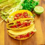 beef tacos with shredded lettuce and tomato salsa stacked together on a wooden board