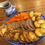 roast beef on a platter with roast potatoes, carrots and yorkshire puddings.