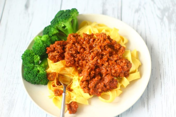 spaghetti bolognese on a bed of pasta with broccoli.