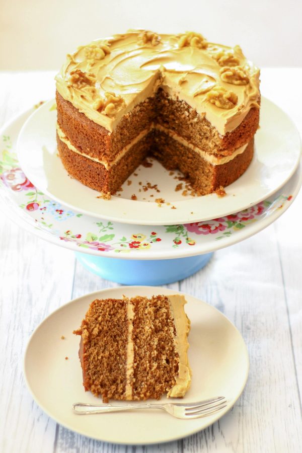 slice of coffee and walnut cake with the original cake in the background