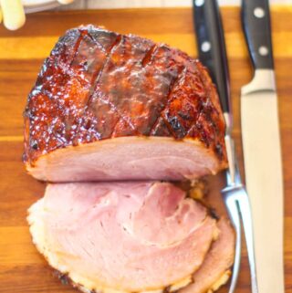 slow cooker gammon joint sliced on a wooden board with carving fork and knife lying alongside