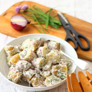 Potato Salad in a bowl with chives and red onion on a wooden board