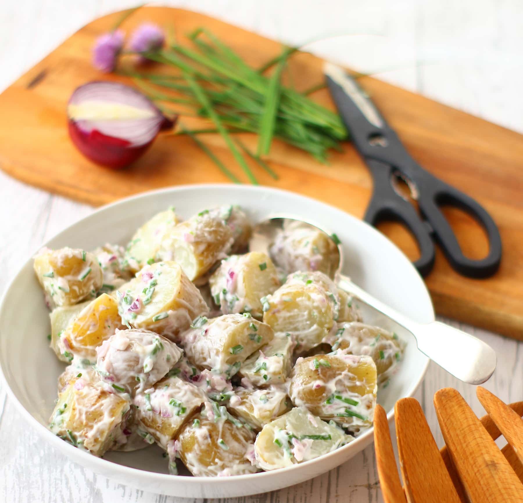 Potato Salad in a bowl with chives and red onion on a wooden board