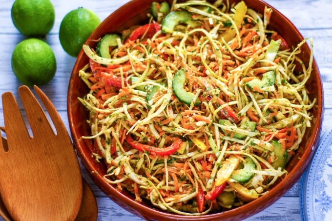 Thai salad in a bowl with salad tongs and limes .