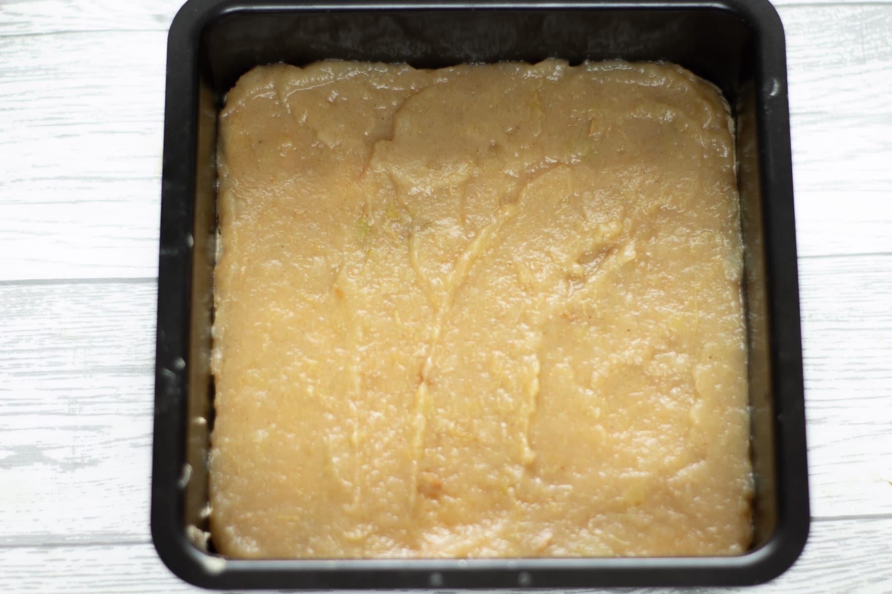 stewed apples spread on a layer of sponge in a cake tin