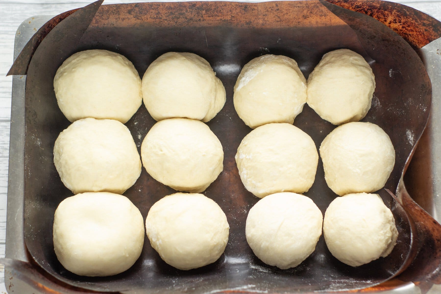 12 bread rolls sitting in a baking tray for their first prove