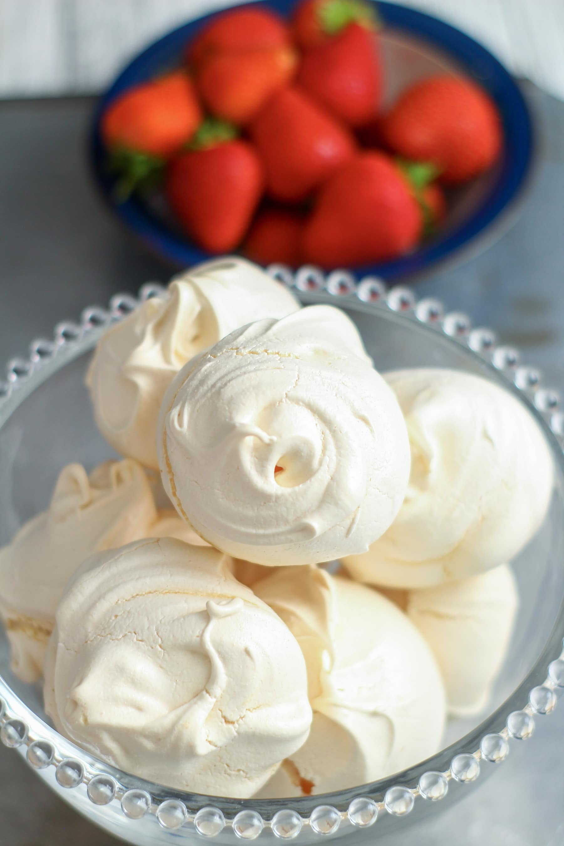 glass bowl filled with meringues, a bowl of strawberries next to it.