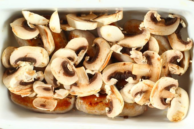 browned sausages and mushrooms in a roasting dish.