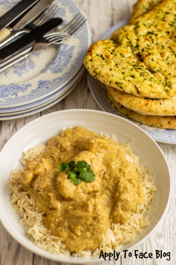 slow cooker chicken curry on a bed of rice in a bowl with some naan breads on the side