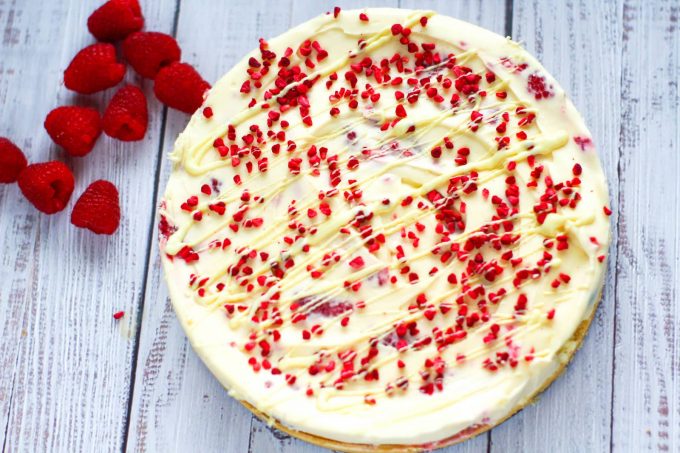 whole white chocolate and raspberry cheesecake decorated with freeze dried raspberries and white chocolate drizzles