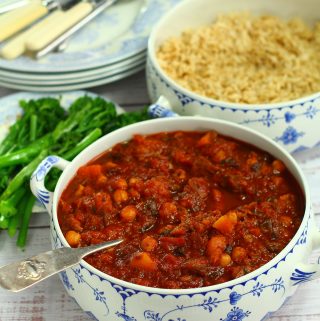 slow cooker moroccan lamb in a serving dish with browned rice and broccoli near by as well as plates and cutlery