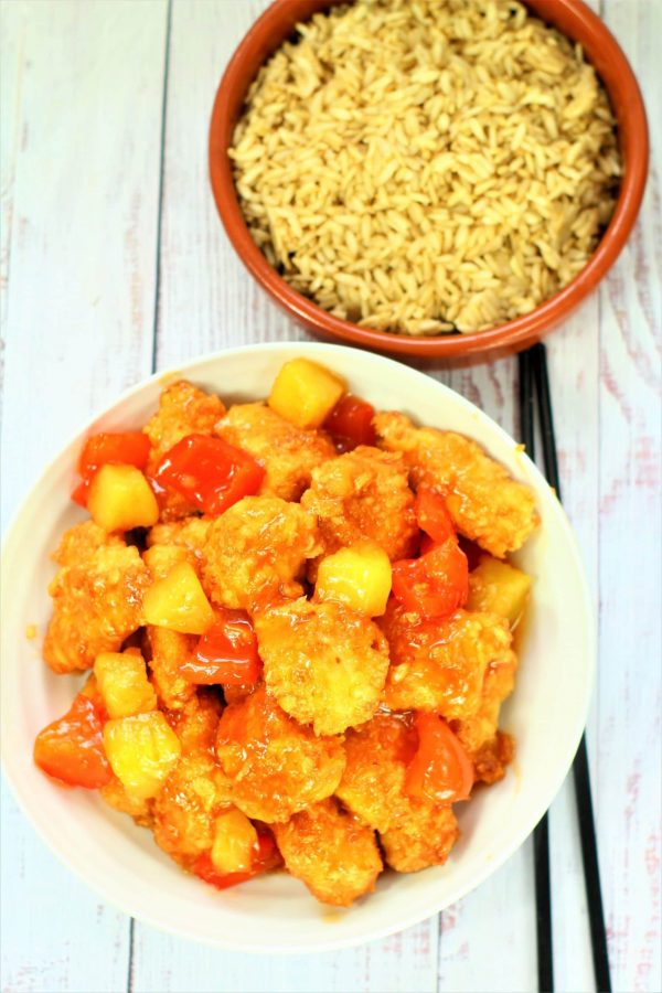 sweet and sour chicken in a bowl with fried rice and chopsticks near by
