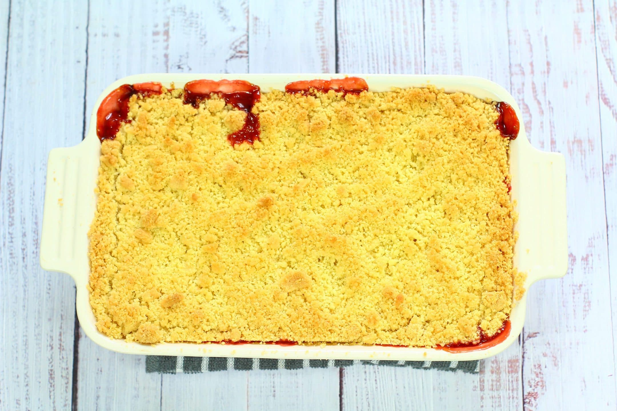 golden brown rhubarb and strawberry crumble with bursts of fruit bubbling through at the edges.