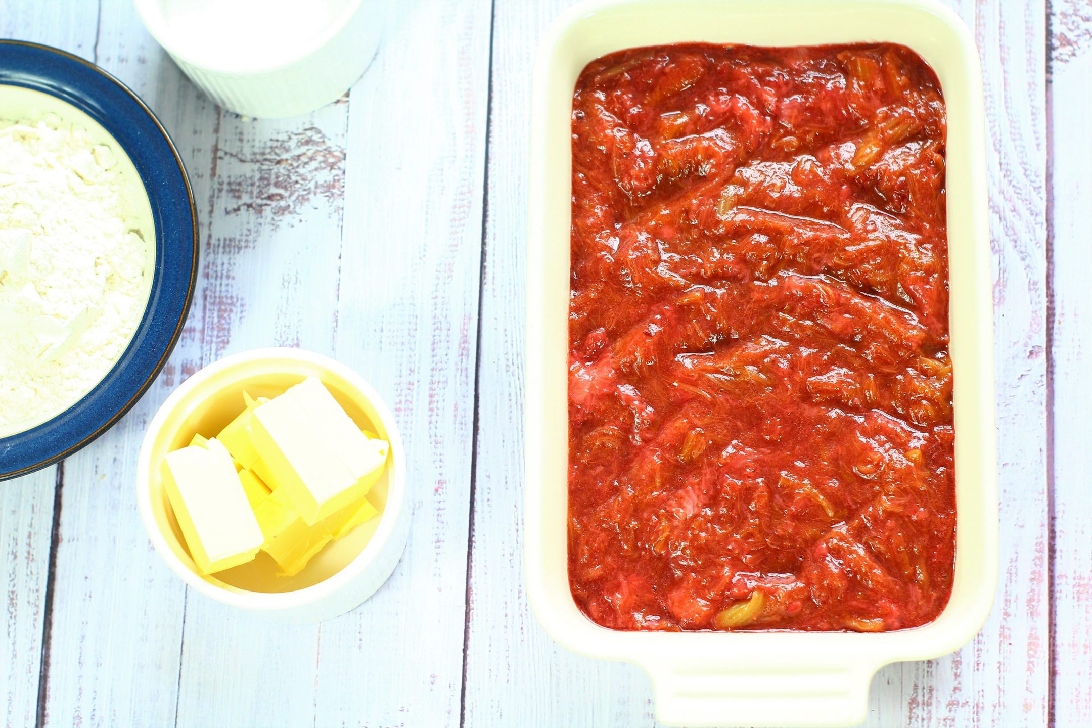 stewed rhubarb in a baking dish with cubes of butter and sugar to the side of it.
