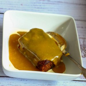 sticky toffee pudding in a white bowl covered in toffee sauce