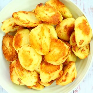 roast potatoes piled up in a white ribbed serving dish