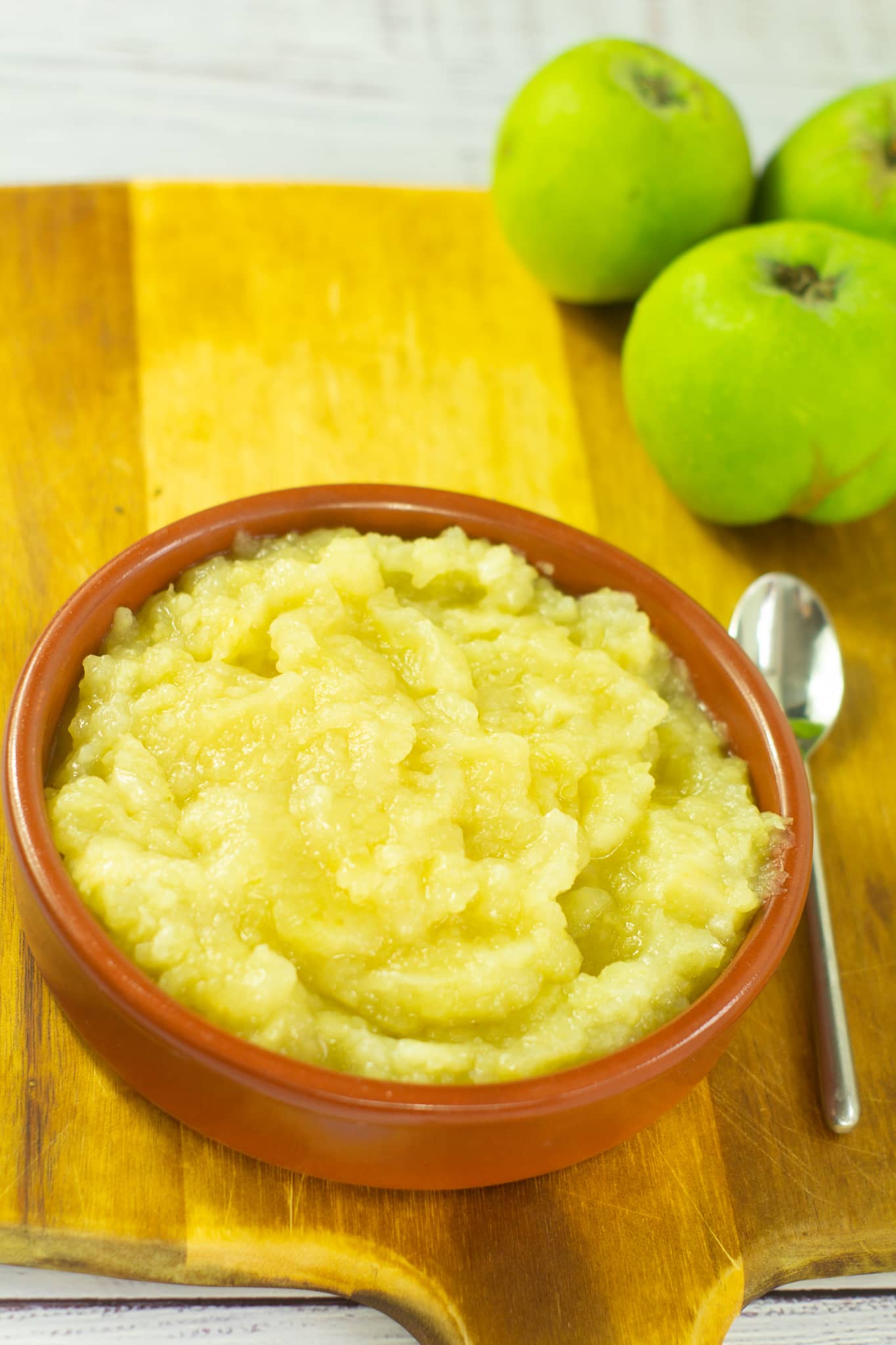 apple sauce sitting in a dish on a wooden chopping board with apples in the background