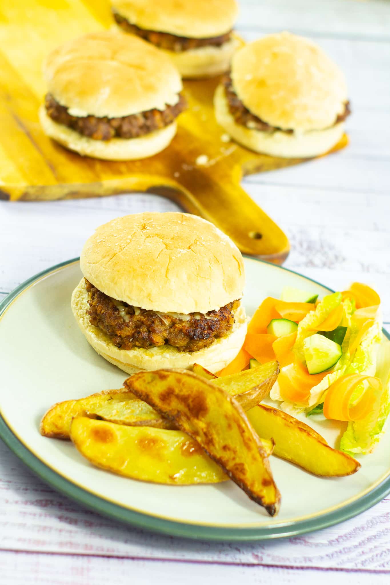 cheeseburger, wedges and salad on a plate with cheseburgers in the background