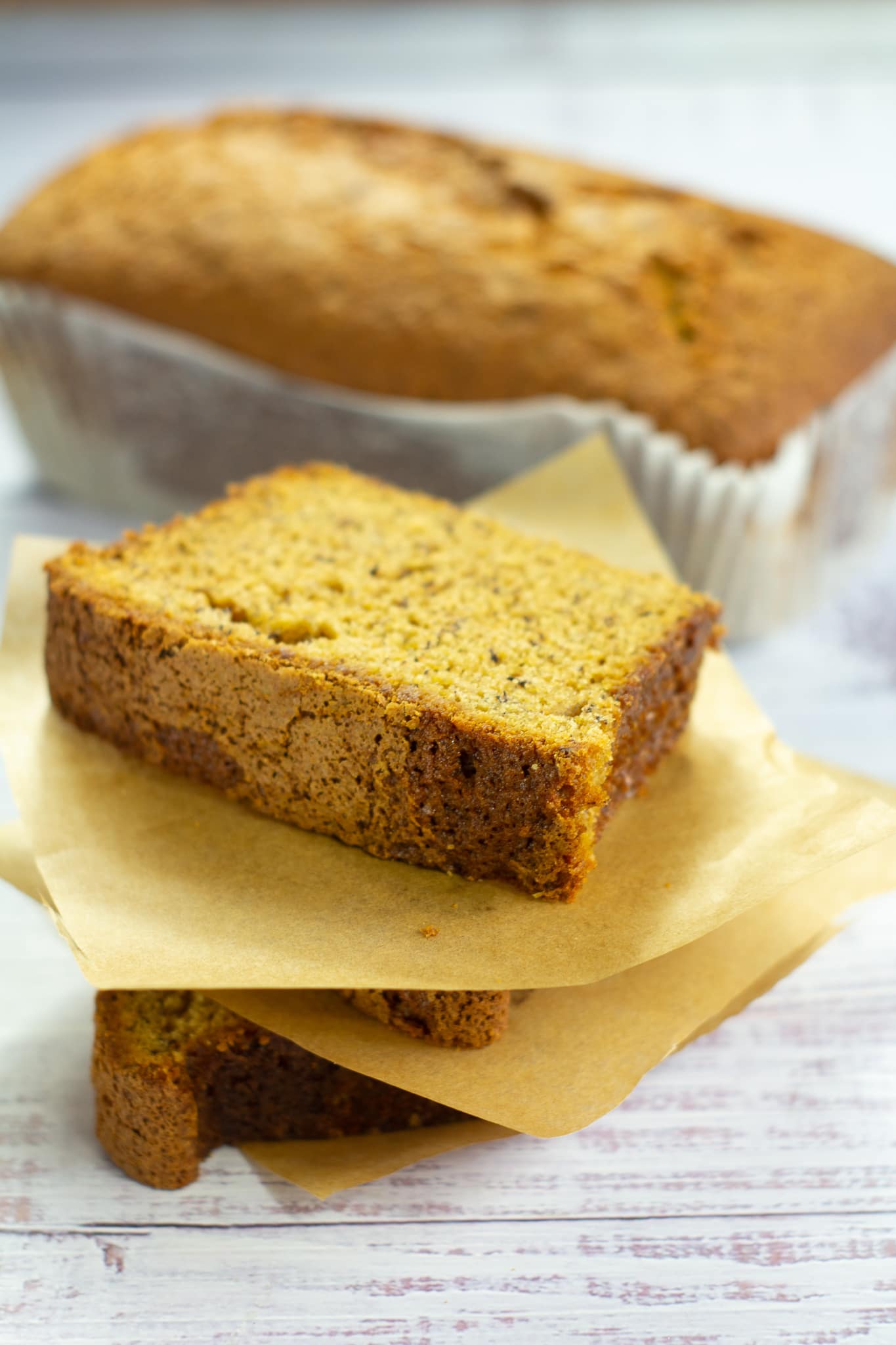 slices of banana bread piled on top of each other with a banana loaf in the background
