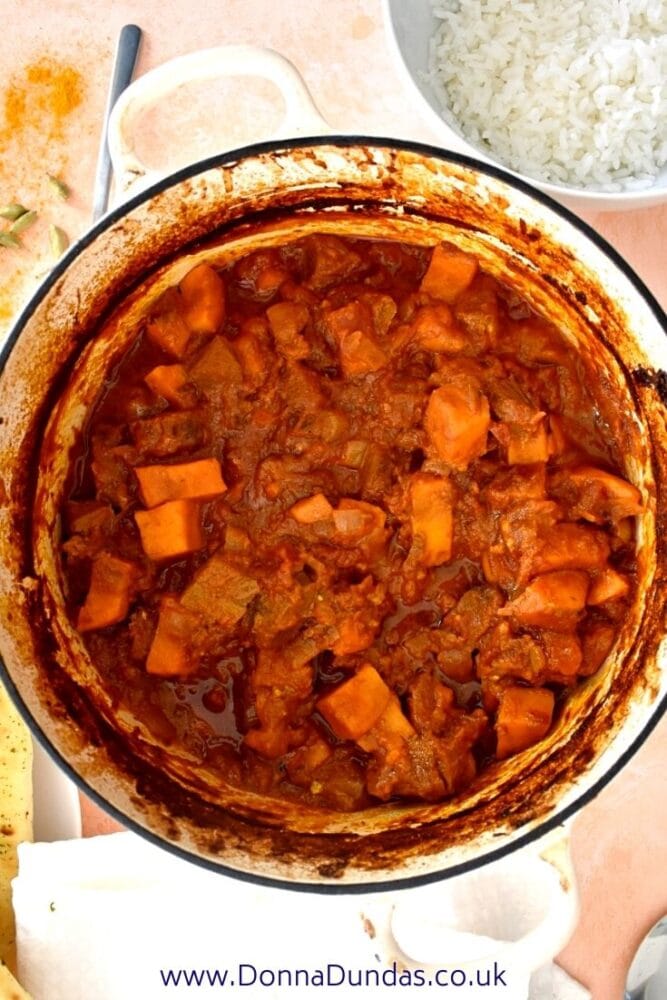 beef and sweet potato curry in a large casserole dish with rice in the background