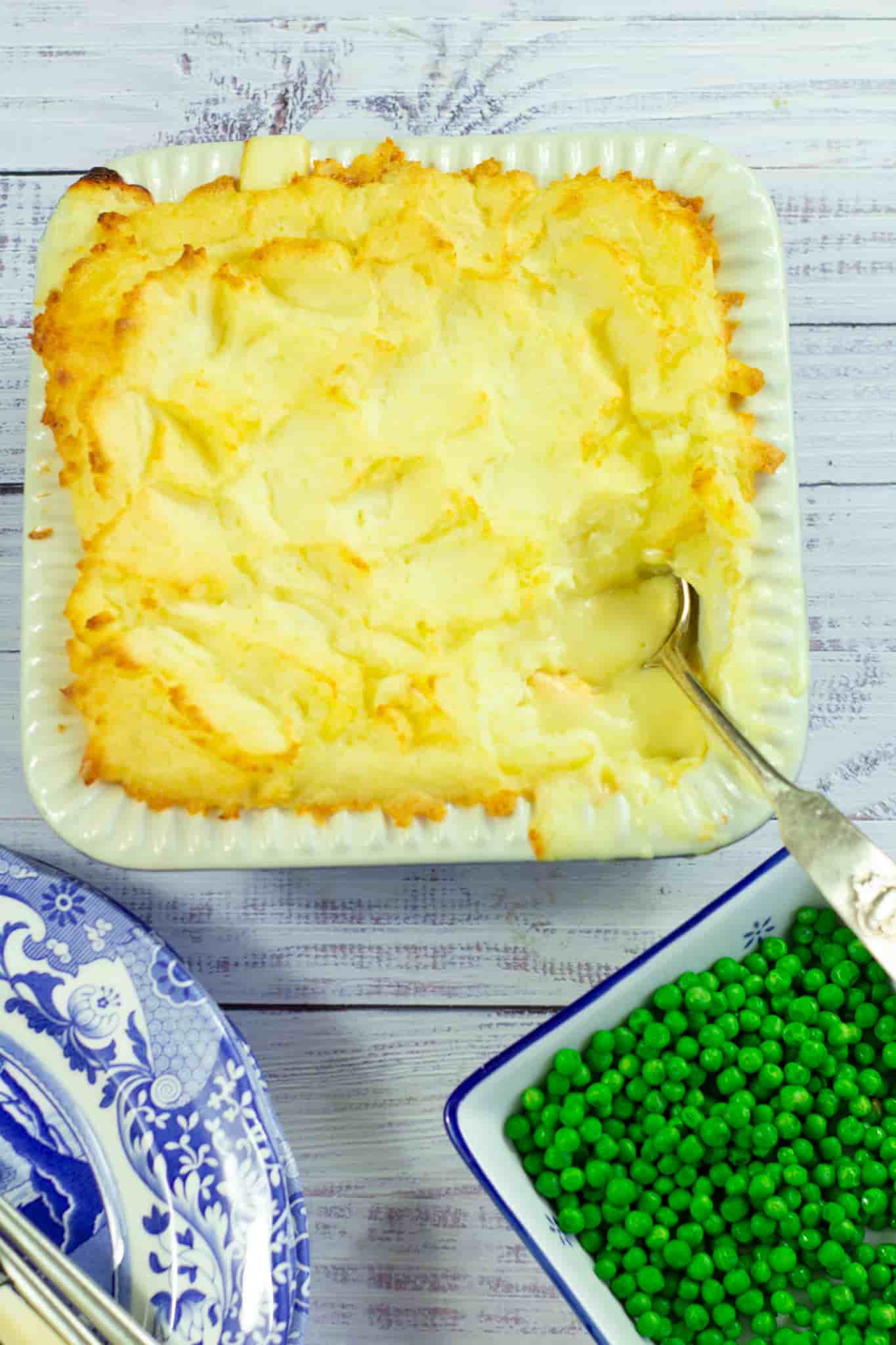 cheesy fish pie with peas to one side and blue and white plates to the other