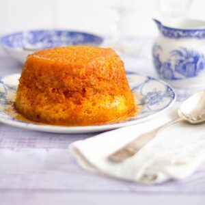 treacle sponge with blue and white crockery set around it. A large serving spoon sits on a white napkin next to it.