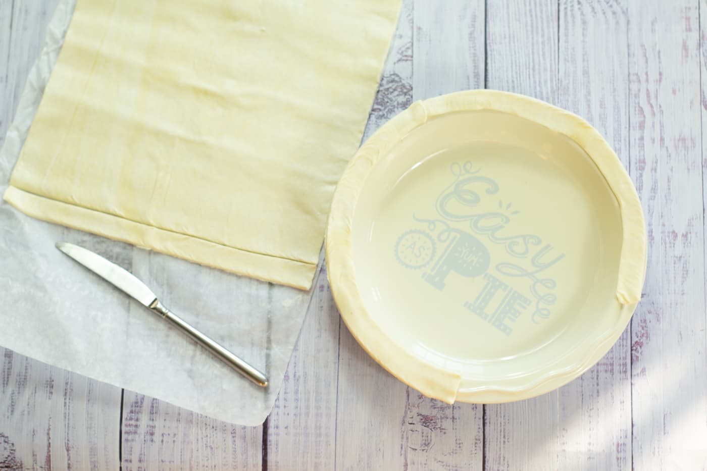 pastry sheet and knife lying next to a pie dish with strips of pastry around the rim.