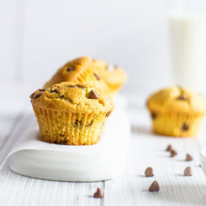 chocolate chip muffins with chocolate chips scattered in the foreground and a glass of milk in the background