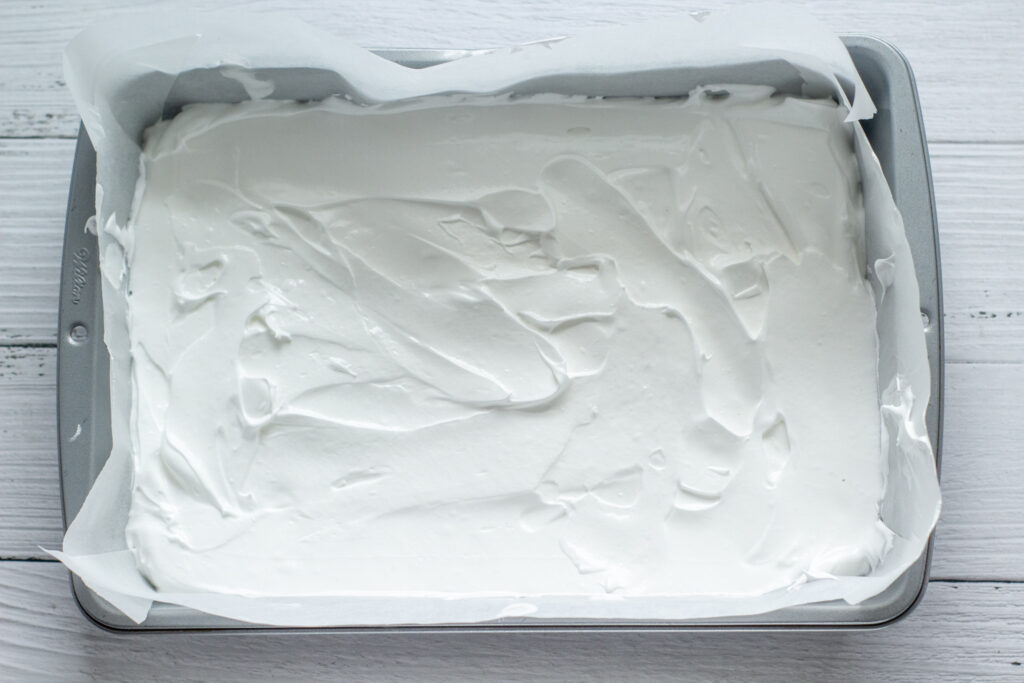 raw meringue spread in a baking tin on a white surface