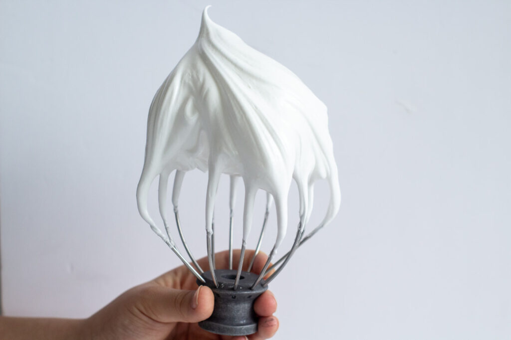 whipped egg white on a metal whisk held upright by a hand.