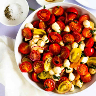tomato salad in a white serving bowl with a small white bowl of salt and pepper to the side