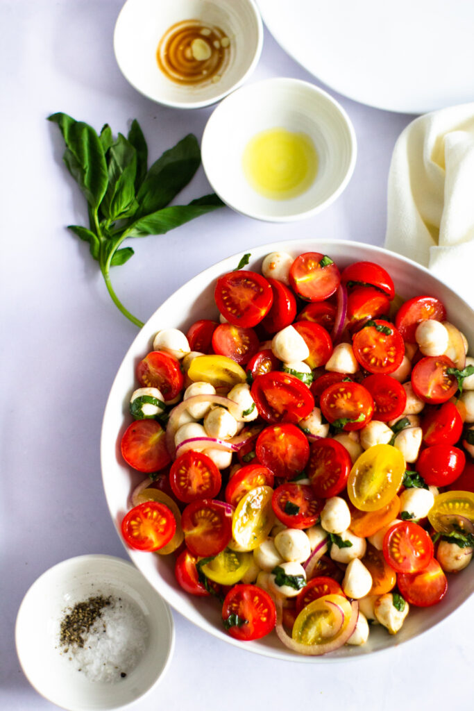 tomato salad in a large white dish with basil and two empty small white pots at the top and a pot of salt and pepper below