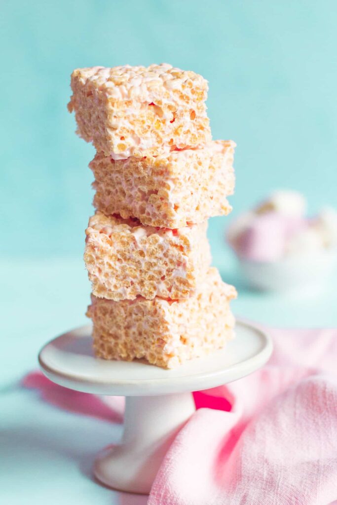 rice krispie marshmallow squares piled high on each other on a small white mini cake stand.