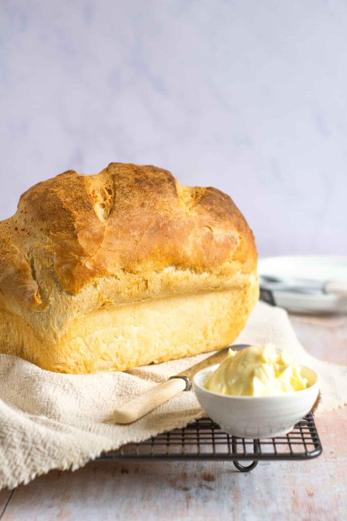 white loaf on a wire cooling rack and a beige napkin with a butter knife