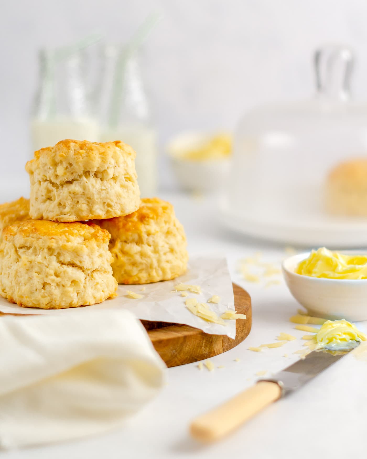 cheese scones stacked on a wooden board with a pot of butter and a butter knife to the side