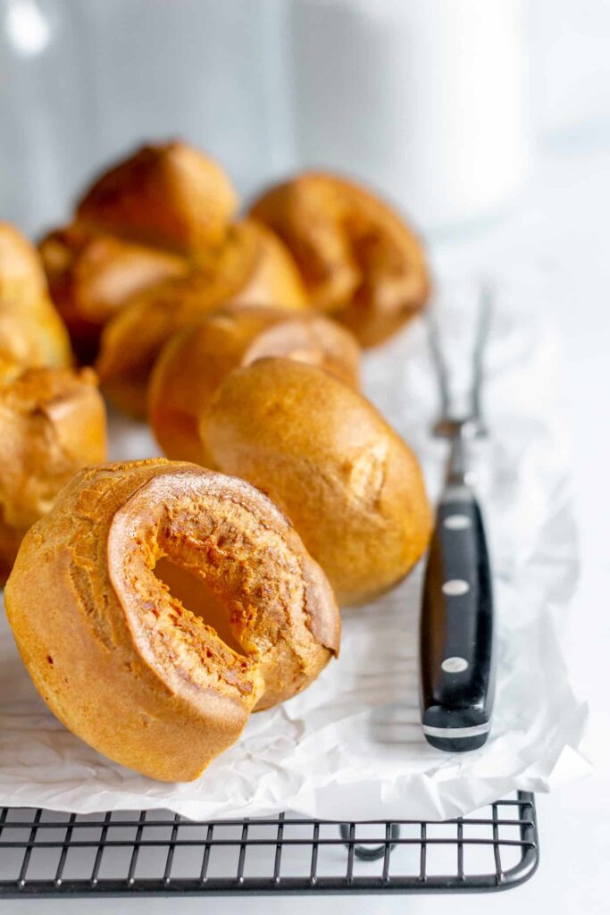 yorkshire puddings on a wire rack and white baking paper with a carving fork to the side