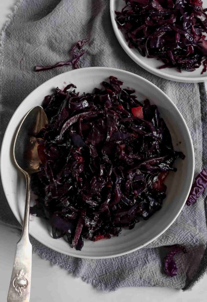buttery red cabbage in a white serving dish on a grey linen napkin and a silver serving spoon