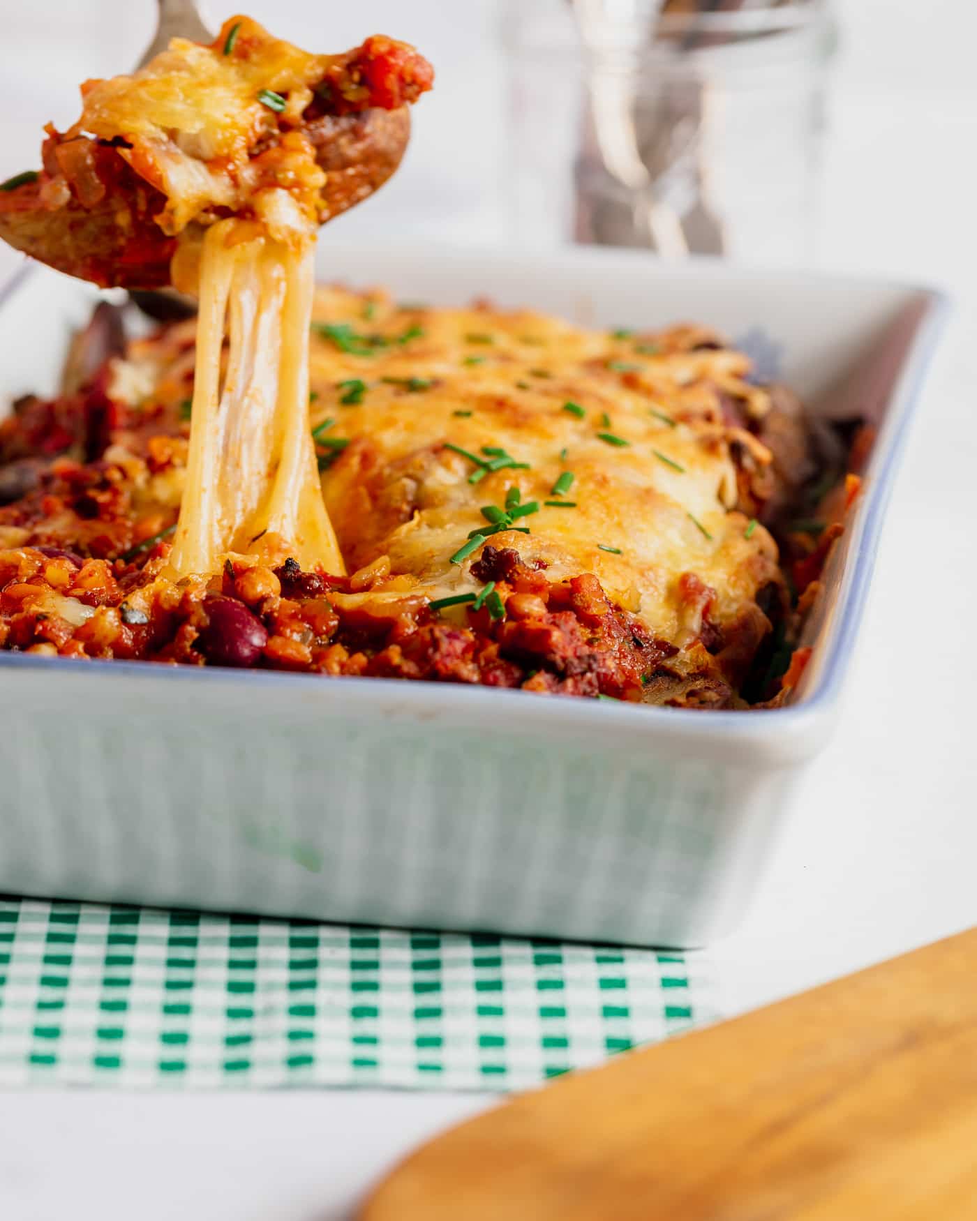 loaded mexican wedges in a white rectangular serving dish. A green and white checked napkin is underneath with a wooden chopping board to the fore. A fork with a wedge and stringy cheese is being pulled from the dish