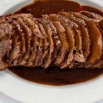 slow cooker roast beef joint sliced on a white plate with gravy poured over it