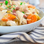 slow cooker chicken casserole with carrots, leeks and chicken in a white serving bowl on a grey and white striped napkin