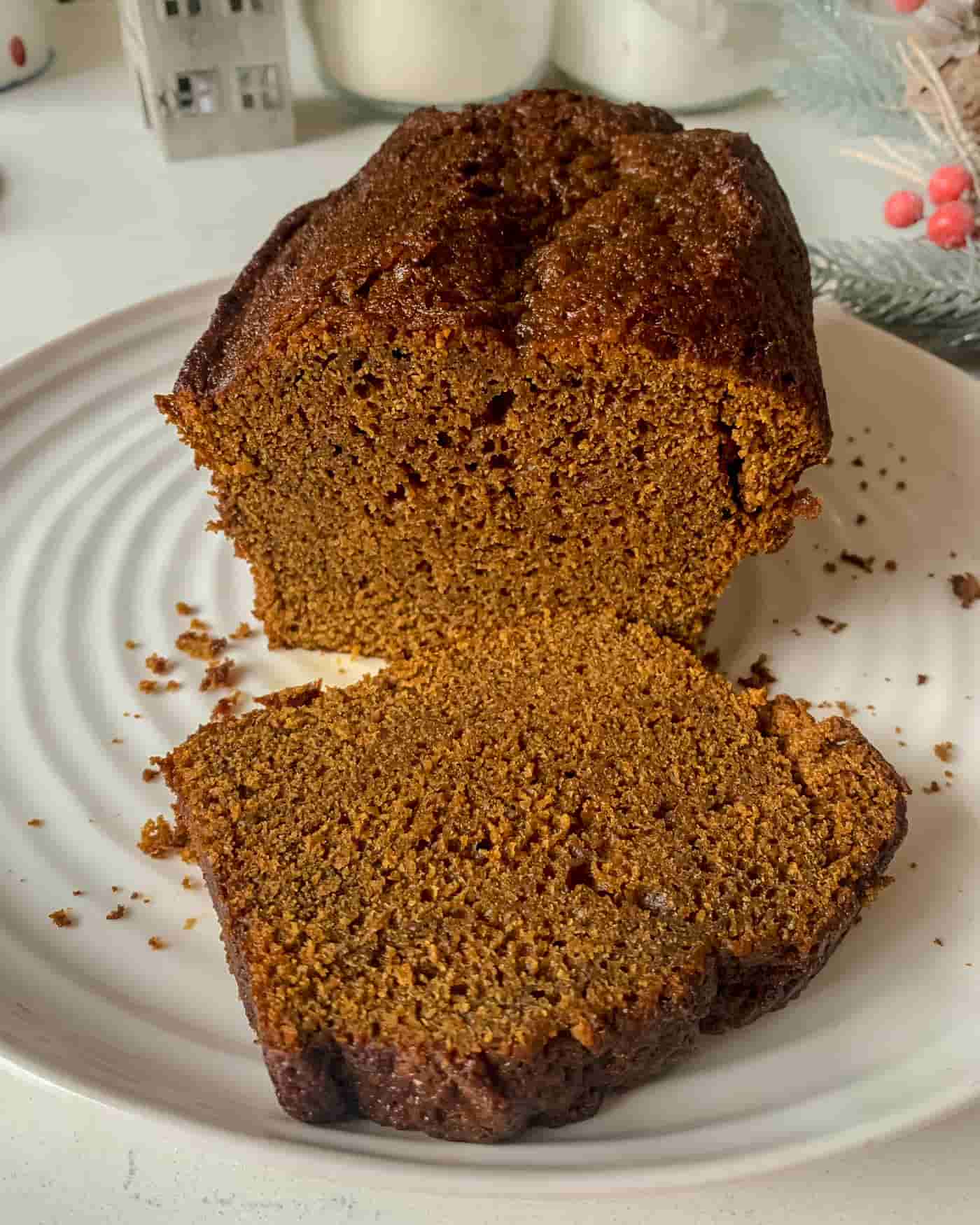 sliced sticky ginger cake loaf on a white serving plate with christmas decorations in the background
