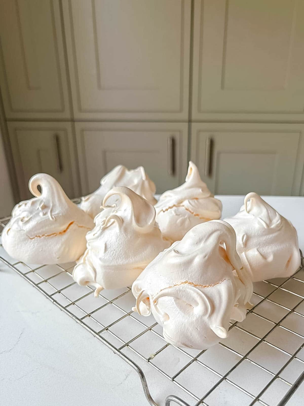 chewy meringues on a wire rack on a white surface with cupboards in the background